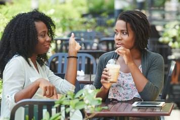 House of Hearing Aids Moab UT - Two black women talking at an outdoor cafe.