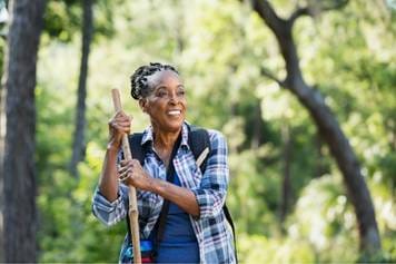 House of Hearing Aids Moab UT - A black woman walking in the woods with a walking stick.